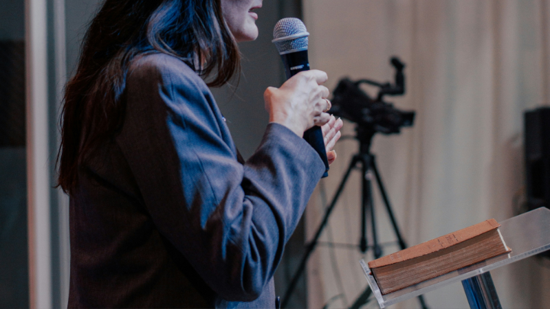 A photo showing a woman speaking at the front of a room.