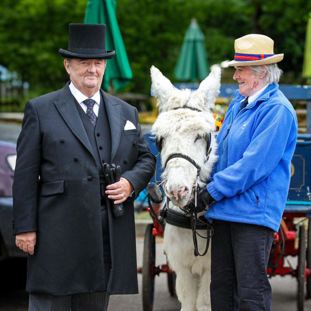 A photo of a CPJ funeral director alongside a donkey for a personalised funeral.